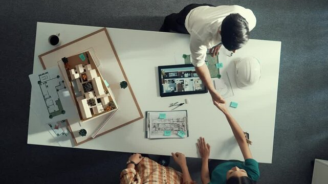 Top view of architect engineer working together and shaking hand cooperative team while making contract and dealing about budget. Aerial view of manager standing and talking about plan. Alimentation.