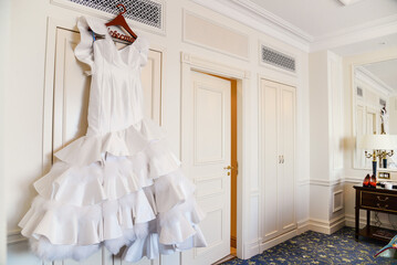 White wedding dress with ruffled skirt hanging in room
