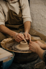 Pottery lesson on a potter's wheel, two people sculpting a shape from clay, hands closeup