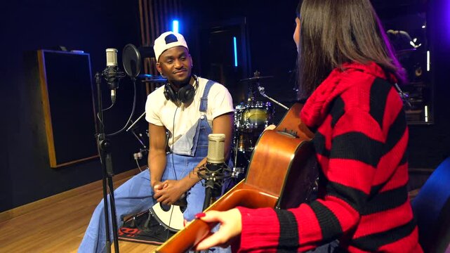 Young female guitarist and male singer collaborating on a new song in a professional recording studio