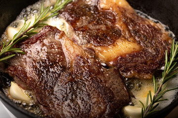 cooking beef steak in a frying pan in butter with garlic and rosemary