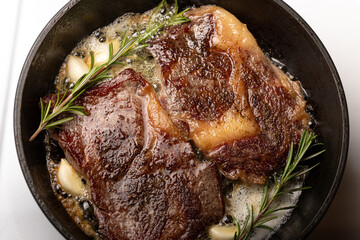 cooking beef steak in a frying pan in butter with garlic and rosemary