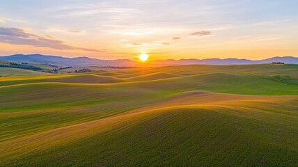 Fototapeta premium Serene sunset over rolling green hills with mountains in distance