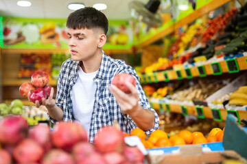 Young man chooses pomegranate fruit on counter of the grocery store