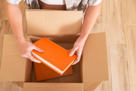 Young woman packing books in a box on wooden floor in moving house