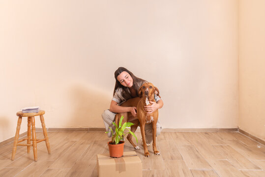 Young Woman Cherishing Her Dog Amidst Moving Boxes and Plant