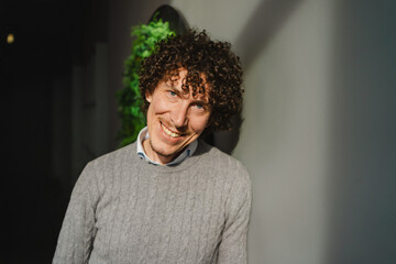 Curly-Haired Man Posing by Green Wall, Embracing Ecology