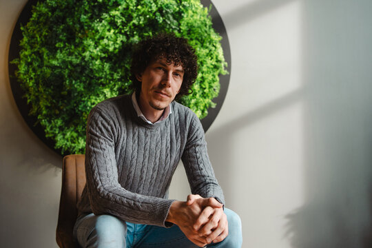 Young man with curly hair sitting by green wall promoting eco themes