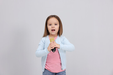 Cute girl with microphone singing near grey wall