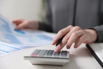Budget. Woman with paperwork and calculator at white desk indoors, closeup