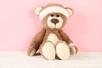 Teddy bear with bandages on white wooden table against pink background