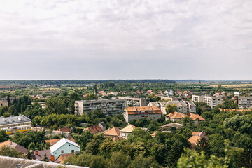Fototapeta premium Scenic vista showcasing a cityscape nestled amidst lush greenery, with rolling hills stretching into the distance under a cloudy sky, offering a tranquil and picturesque view