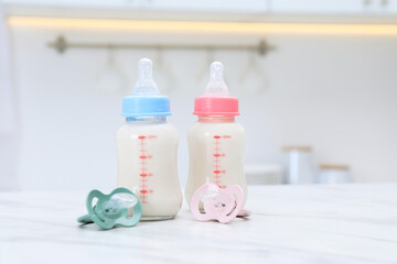 Feeding bottles with baby formula and pacifiers on white table indoors