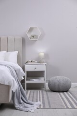 Stylish bedroom interior with knitted pouf and furniture