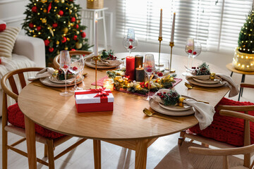 Christmas table setting with stylish dishware, glasses and burning candles in festive decorated room