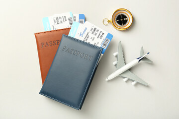 Passports with tickets, plane model and compass on light background, flat lay