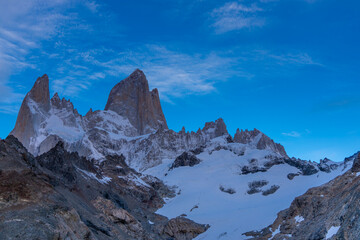 Fototapeta premium Fitz Roy sharp mountain peaks rise above a serene glacial lake, surrounded by rugged terrain snow-covered slopes in Patagonia, Argentina, El Chalten. Fitzroy mountain granite peak laguna de Los Tres