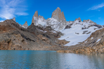 Obraz premium Fitz Roy sharp mountain peaks rise above a serene glacial lake, surrounded by rugged terrain snow-covered slopes in Patagonia, Argentina, El Chalten. Fitzroy mountain granite peak laguna de Los Tres