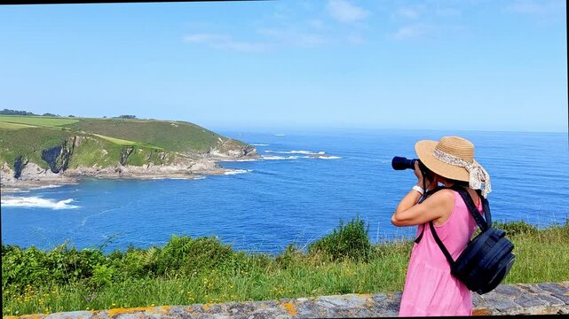 Tourist woman taking photographs at Busto cape, Asturias, Spain