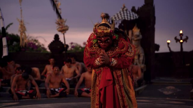 Bali, Indonesia : Red-robed performer dominates temple stage while chorus creates hypnotic atmosphere at twilight during kecak ramayana performance