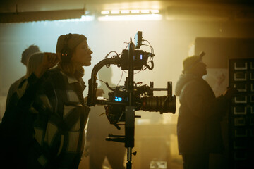 The director of photography is a woman behind a video camera on the set. A professional videographer at work on the filming of a movie, commercial or TV series. Filming process indoors, studio