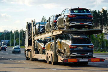 Truck carrying new cars on hauler trailer, logistics services, freight transportation industry. Car hauler semi-truck carrying batch of new cars for sale, automotive transport and freight logistics.