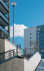 Fototapeta premium Modern Urban Staircase with Railings, Residential Buildings, and Lamp Post Under a Blue Sky