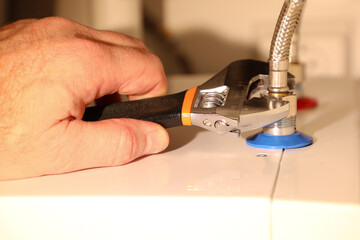 To connect the hot and cold water hoses to the boiler, an experienced plumber uses an adjustable wrench.