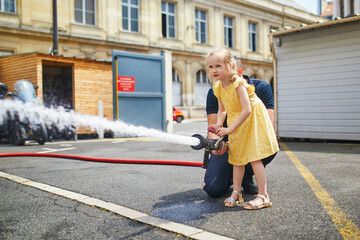 Fototapeta premium preschooler girl acting like a fireman holding firehose nozzle and splashing water