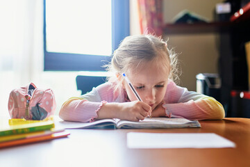 Tired little girl doing her homework for school at home.