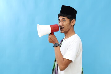 Fototapeta premium Asian muslim man announcing on megaphone isolated on blue background