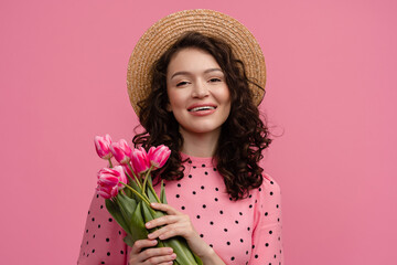 pretty young woman posing isolated on pink studio background with tulips flowers