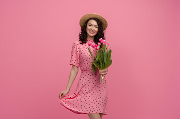 pretty young woman posing isolated on pink studio background with tulips flowers