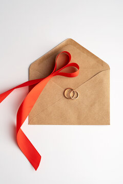 Top view of wedding rings on an envelope with a red ribbon