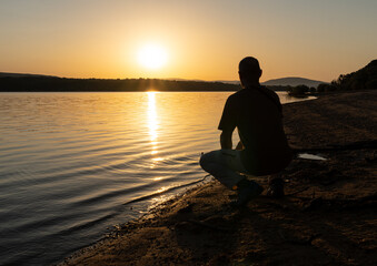 silhouette of man meditating on lake at sunset