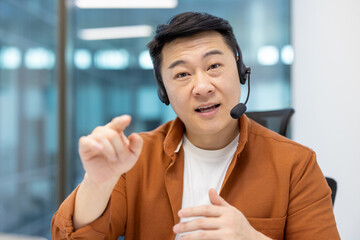 Webcam view, man with headset looking into camera, talking and consulting clients remotely. Support service worker at workplace inside office, using video call, for business conference meeting.