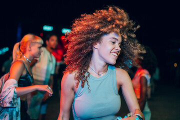 Carefree young woman dancing with friends at night music festival