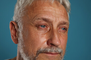 Sad senior man crying on blue background, closeup