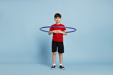 Boy exercising with hula hoop on light blue background