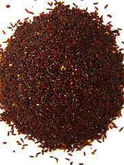 Fototapeta premium Pile of dark brown unprocessed rice grains with a reddish hue scattered on a white background viewed from above.
