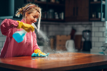 Woman cleaning wooden kitchen countertop with spray