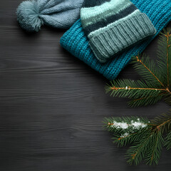 Soft blue knitted wool winter hats with snow covered pine branches on rustic wooden background