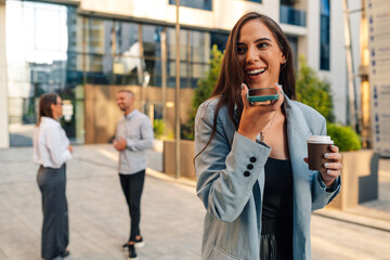 Businesswoman recording voice message while holding coffee outside office building