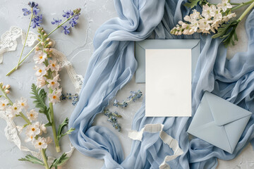 A beautifully arranged flat lay features wedding invitation cards atop a soft blue fabric, accompanied by vibrant flowers and decorative lace