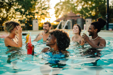 Friends enjoying drinks in swimming pool at sunset during summer party