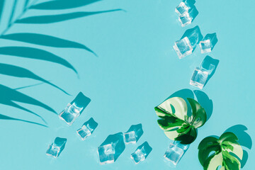 Summer day scene with ice cubes, palm leaf shadow and tropical monstera leaves on blue background. An original backdrop image with a play of light and shadow. Minimal concept. Flat lay. Copy space.