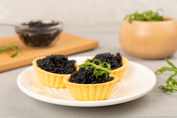 Tartlets with black caviar served on on wooden table