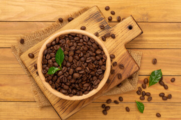 Roasted coffee beans with leaves on wooden background,top view