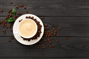 Cup of coffee with coffee beans and leaves on wooden background,top view