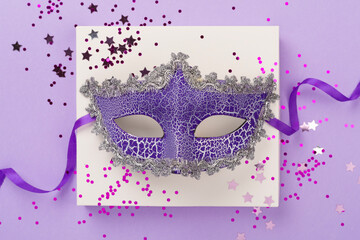 Bright carnival mask with confetti on color background, top view